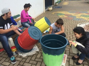quatro estudantes pintando lixeiras de cores diferentes