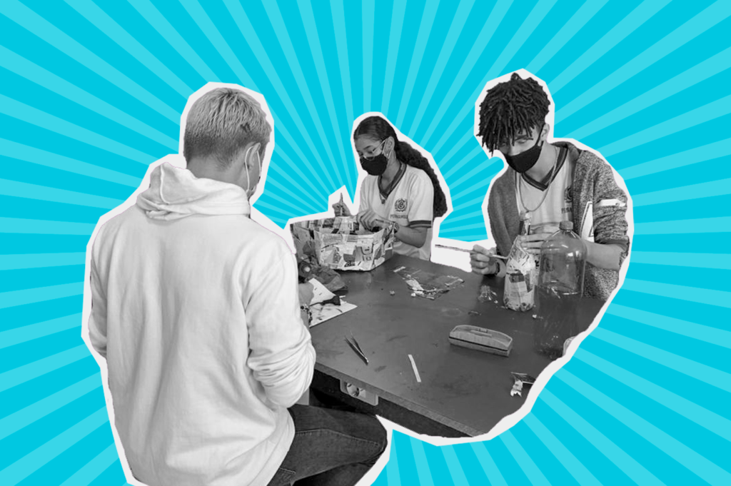 foto em preto e branco de três adolescentes num fundo azul - dois meninos um branco e outro negro e uma menina de negra - sentados à mesa, fazendo um armário reciclado com papel e garrafa pet.