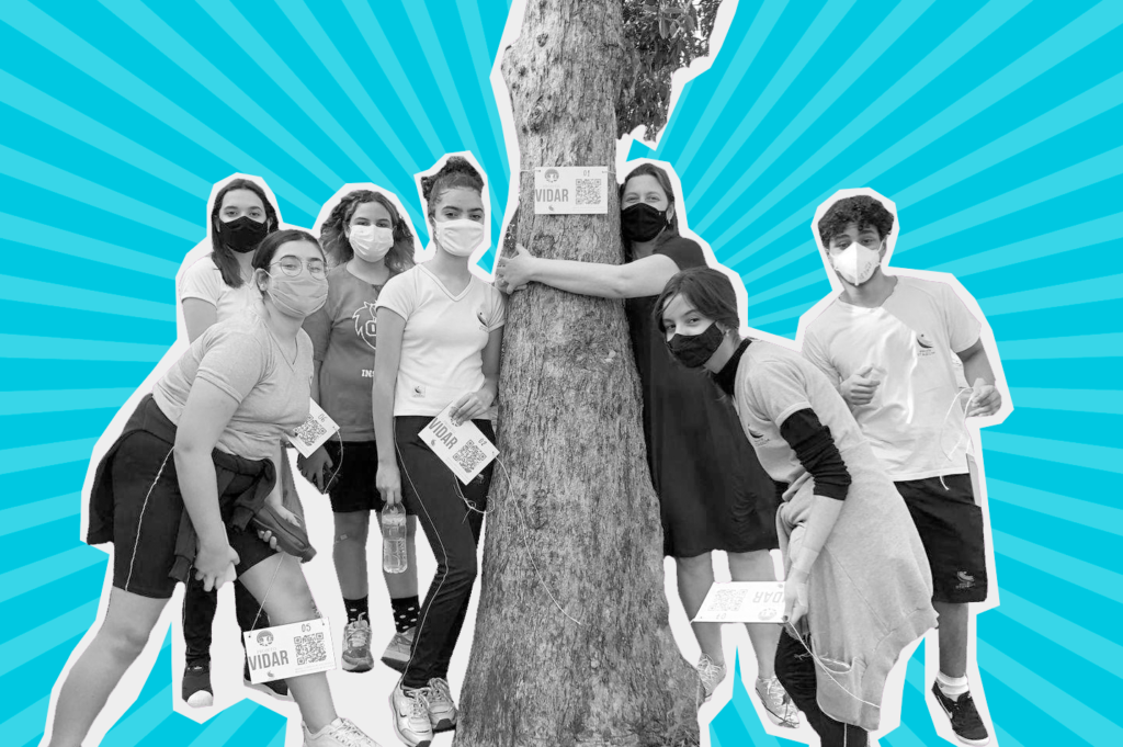 Arte com fundo azul e foto recortada em tons de cinza de uma grupo 6 adolescentes e uma mulher adulta ao lado de uma árvore. Todos usam máscara de proteção.