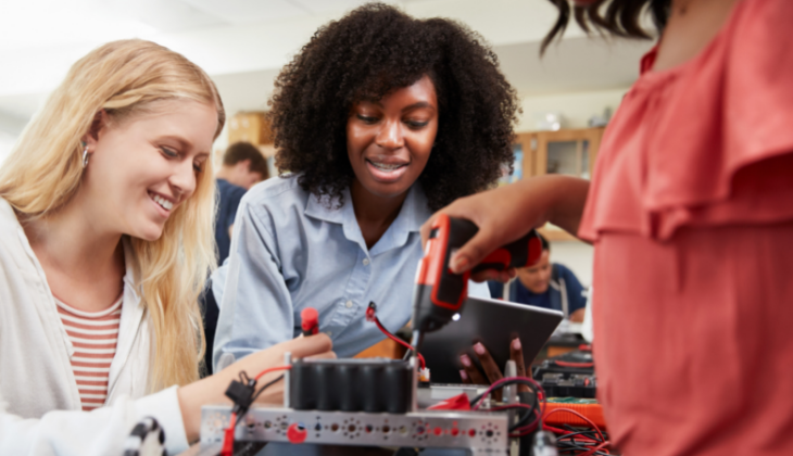 foto de duas meninas - uma branca e uma negra - e uma mulher negra mexendo em um equipamento eletrônico