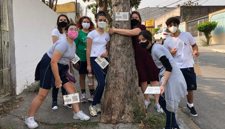 foto de um grupo de adolescentes e uma mulher usando máscara e abraçando um árvore